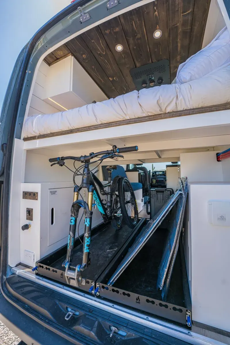 Backside of Papago Vans custom Mercedes Sprinter build with a bed lift above storage room for a mountain bike with equipment storage cabinets and heavy duty pull out trays to easily access the bikes.