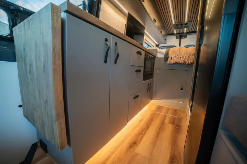 Grey kitchen cabinets with leather pulls and warm floor lighting along the aisle